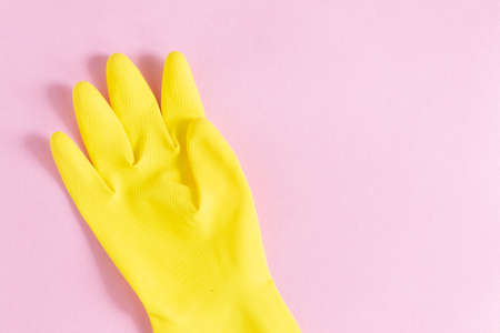 A closeup shot of a yellow plastic glove on a pink background