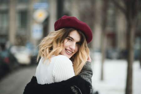 A shallow focus shot of an attractive happy blonde female in warm winter clothes posing on the streetの写真素材