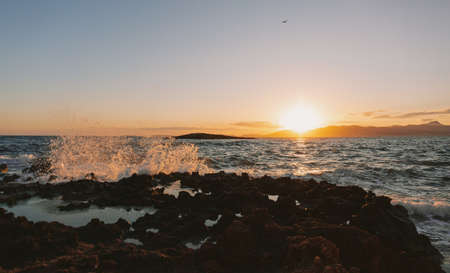 A wide shot of rock formations in the wavy ocean during sunset under the clear sky