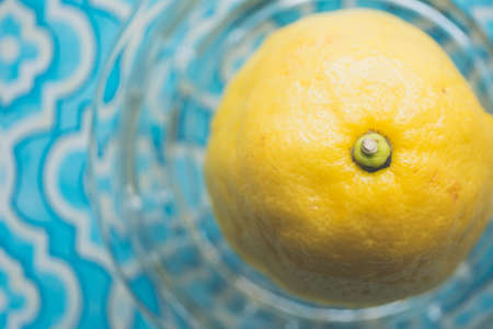 A closeup shot of a whole lemon in a glass container on a patterned blue wallpaper backgroundの写真素材