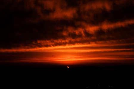 A silhouette of mountains under an orange cloudy sky