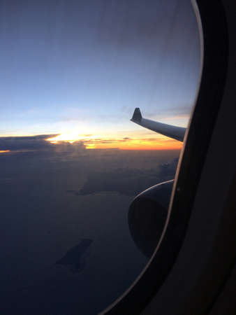 A vertical shot of an airplane window with a view of the wing and a blue sky