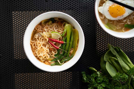 An overhead shot of soup with noodles and vegetables in a white bowl