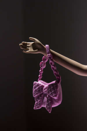 A vertical closeup shot of a plastic doll's hand holding a pink purseの写真素材