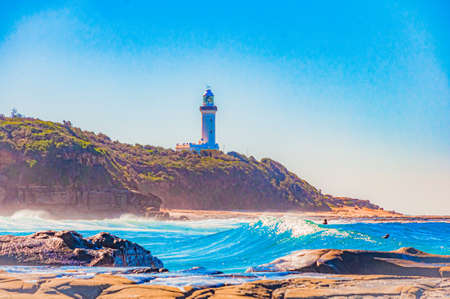 A beautiful shot of ocean waves and a beacon light tower on a cliff in the backgroundの写真素材
