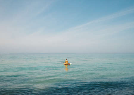 A beautiful shot of a female on a paddle boat holding an oar in the water with a clear sky in the backgroundの写真素材
