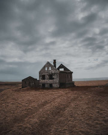 A beautiful shot of an old abandoned and half-destroyed house in a large brownfield under the gray...