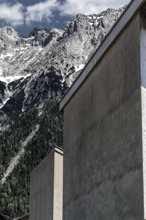 A vertical shot of gray buildings near mountains surrounded by treesの写真素材