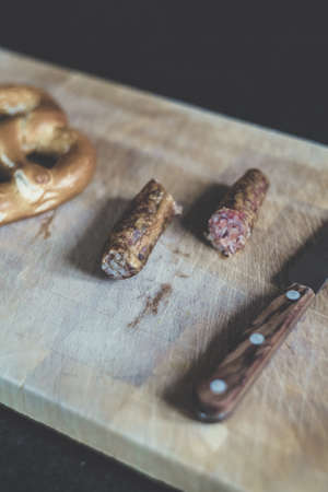 A high angle shot of sliced sausage beside brown handle knife and a piece of bread on a wooden chopping boardの写真素材