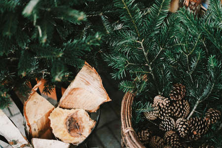 A close shot of chopped wood in a bucket near a basket full of pine tree branches and pine conesの写真素材