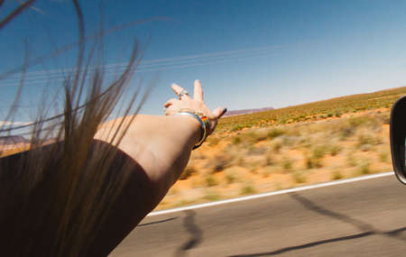 A female waving her hand out of the car's window on a sunny dayの写真素材