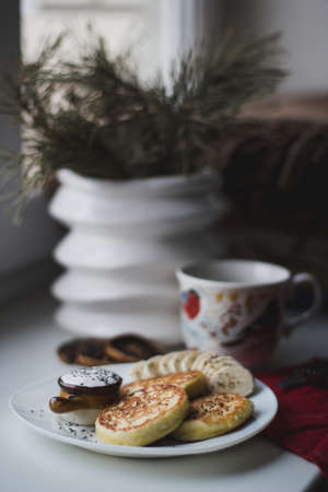 A vertical selective shot of pancakes and sliced bananas on a plate near a teacup and flower pot on...