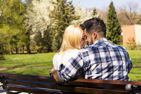 A happy loving caucasian couple sitting on a park bench, flirting on a sunny dayの写真素材