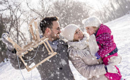 A happy caucasian family in a snowy field, the mother holding their daughter, and the father holding...