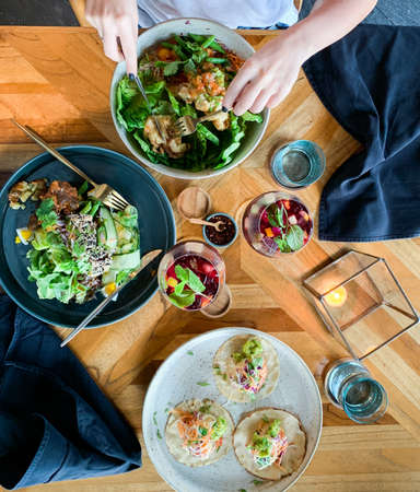 A vertical overhead shot of a person eating organic salads near a table filled with glasses with...