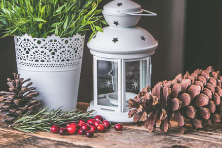 A closeup shot of red coffee beans and a pinecone with a candle lantern on a wooden surfaceの写真素材