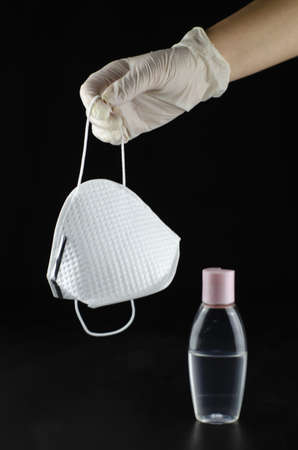 A vertical shot of a person holding a mask with a bottle of hand sanitizer isolated on a black backgroundの写真素材