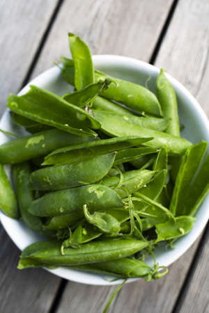 A vertical high angle shot of a bowl of snow pea's peels on a wooden tableの写真素材