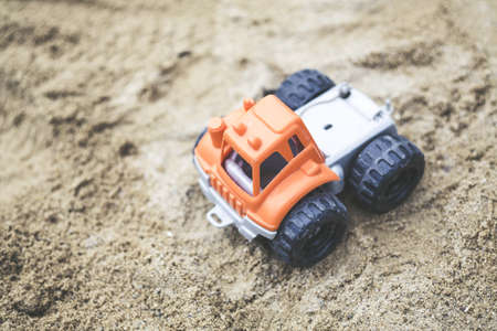 A shallow focus shot of an orange truck plastic toy on the sand on a sunny dayの写真素材
