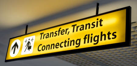 A yellow and black "Transfer, Transit, Connecting flights" information board sign at airportの写真素材