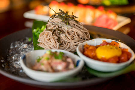A close shot of noodles with vegetable leaves near side dishes on a plate with a blurred backgroundの写真素材