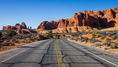 A beautiful shot of an empty road in the middle of a desert with bushes and cliffs in the distance under a blue skyの写真素材