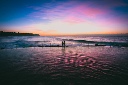 A silhouette of a young couple admiring the view of the sea at seashore under the breathtaking colorful skyの写真素材