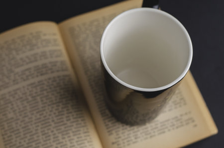 A high angle shot of an empty cup with an open book backgroundの写真素材