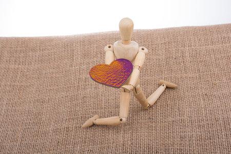 A little wooden male toy holding a heart-shaped object - concept of making a proposalの写真素材