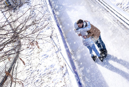 A happy couple hugging while ice skating and enjoying the snowfall at the ice rink in the park in winterの写真素材