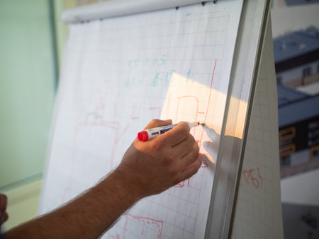 A selective closeup shot of a person holding red marker pen writing on a whiteboardの写真素材