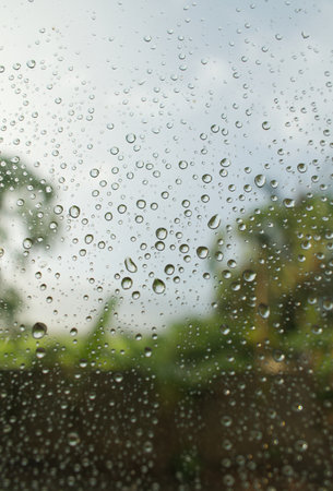A vertical selective focus shot of the raindrops on a window with a blurred natural background