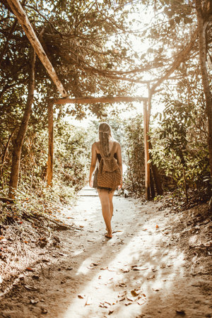 A vertical shot of a woman with a backpack walking amongst the trees barefootの写真素材