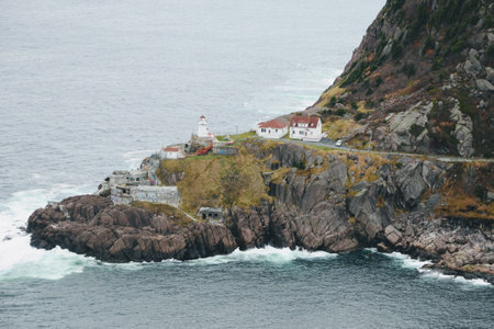 A bird's-eye shot of a shore with houses and a lighthouse, the sea visible in the distanceの写真素材