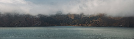 A horizontal shot of mountains by the body of the sea covered in fogの写真素材