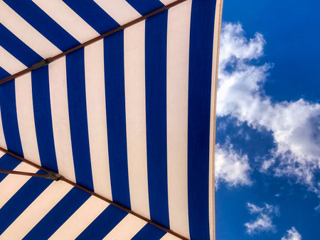 A relaxing wallpaper with striped blue and white textured parasol and cloudy blue sky in the backgroundの写真素材
