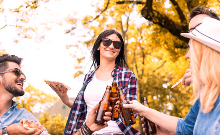 A cheerful group of caucasian friends drinking beer and eating pizza in a parkの写真素材