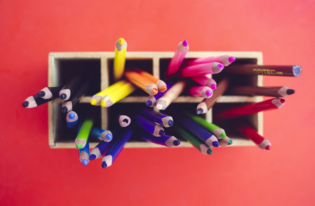 A high angle shot of colorful coloring pencils in wooden case on a pink surfaceの写真素材