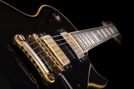 A shallow focus closeup shot of a black electric guitar in front of a black backgroundの写真素材