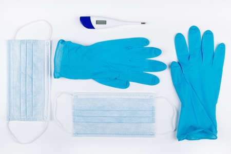A high angle shot of two surgical masks, a pair of gloves, and a digital thermometer on a white...