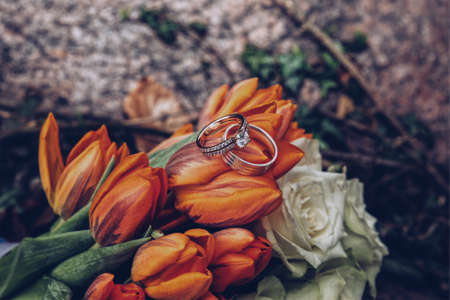 A selective closeup shot of silver diamond rings on orange tulips and white rosesの写真素材