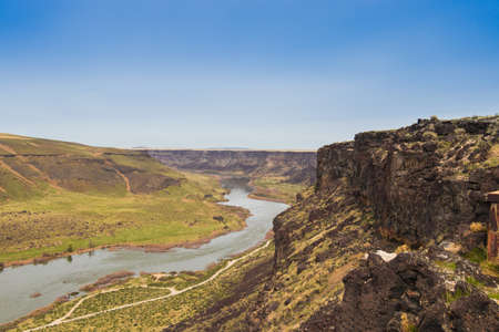 A wide shot of a river flowing between mountains and hills under a clear blue sky