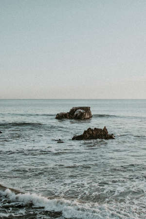 A vertical shot of the beautiful sea with a rock formation in the middle on a cloudy day