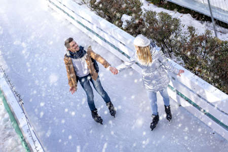 A happy couple ice skating and enjoying the snowfall at the ice rink in the park in winter