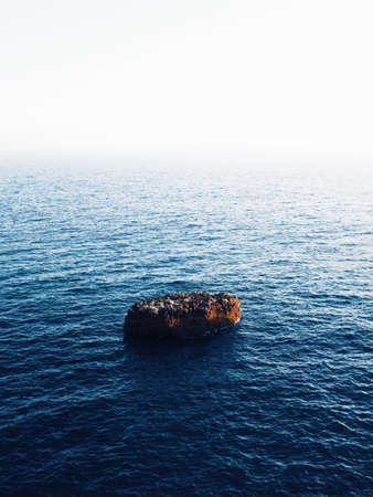 A beautiful vertical shot of a brown rock in the middle of the sea with amazing water texturesの写真素材