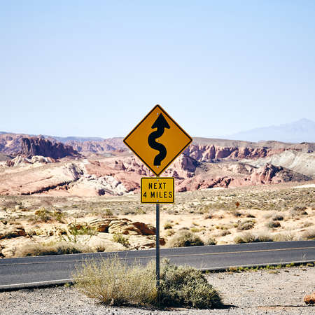 A yellow curve road sign on the road surrounded by rocky mountains  in the Valley of Fire, Nevada under the beautiful blue skyの写真素材