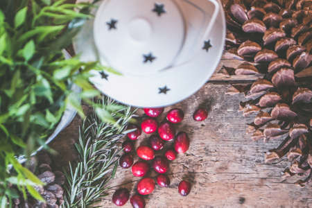 A closeup shot of red coffee beans and a pinecone with a candle lantern on a wooden surface