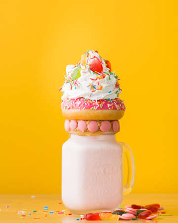 A vertical closeup shot of a dessert with a doughnut and whipped cream on a drinking jarの写真素材