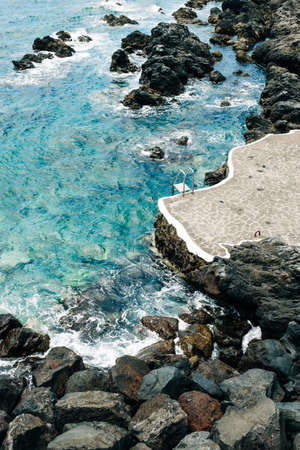 A vertical shot of the sea surrounded by rocks under the sunlight - perfect for wallpapersの写真素材