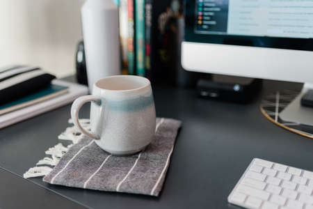 A selective focus shot of a white cup on a desk near a computer at an officeの写真素材
